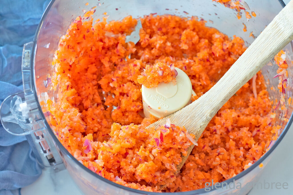 Minced onion, carrot and celery in the bowl of a food processor after being processed.