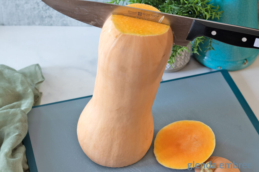 Whole butternut squash with ends removed standing upright on a cutting board to be sliced in half vertically.