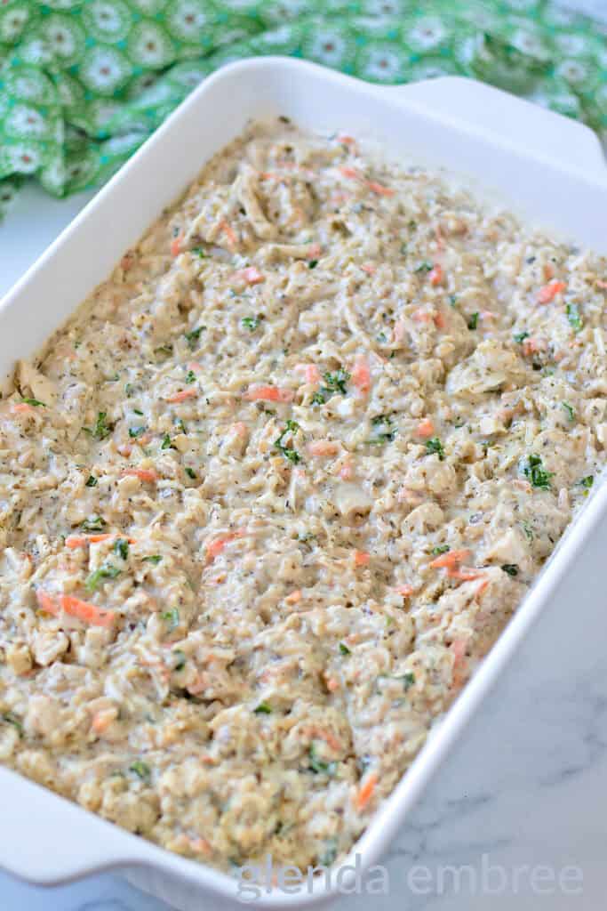 Pesto Alfredo Chicken and Rice ingredients mixed in a white ceramic baking dish.