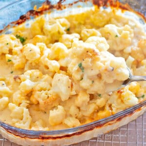 Baked Cauliflower Gratin, (Cauliflower with Cheese Sauce), Cauliflower Cheese, Cheesy Cauliflower in a clear glass baking dish with a sprinkle of chopped parsley.