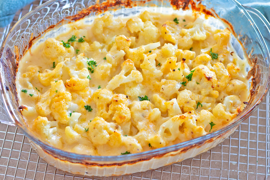 Baked Cauliflower Gratin, (Cauliflower with Cheese Sauce), Cauliflower Cheese, Cheesy Cauliflower in a clear glass baking dish with a sprinkle of chopped parsley.