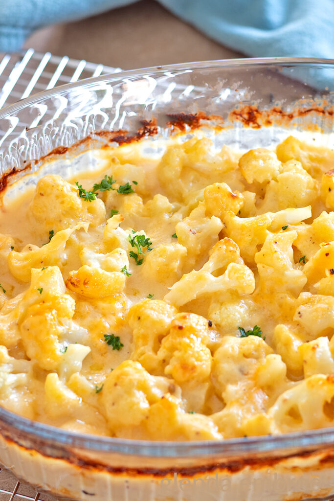 Baked Cauliflower Gratin, (Cauliflower with Cheese Sauce), Cauliflower Cheese, Cheesy Cauliflower in a clear glass baking dish with a sprinkle of chopped parsley.