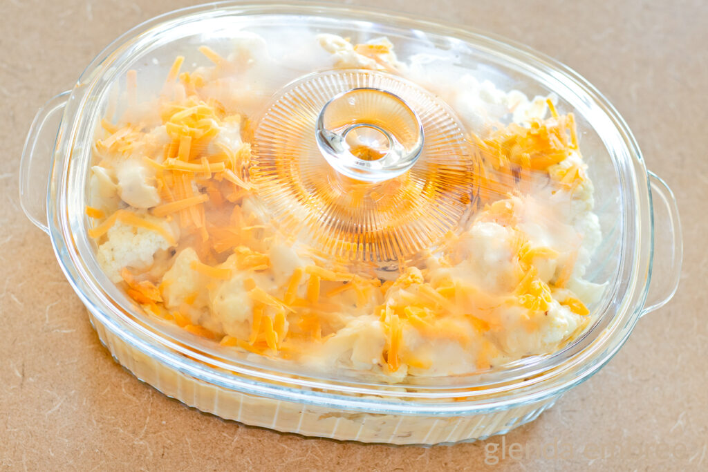 Cauliflower gratin mixture in a clear glassing baking dish with a lid.