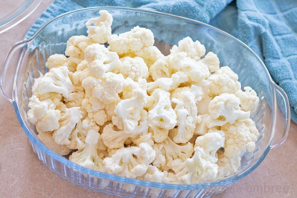 Raw cauliflower florets in a clear glass baking dish.