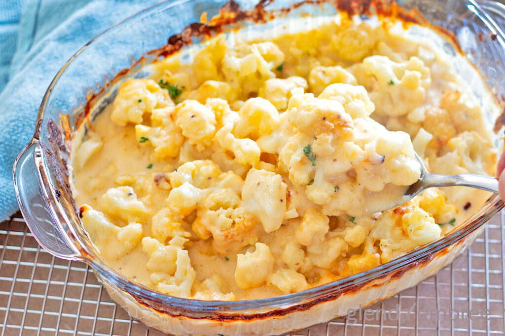 Baked Cauliflower Gratin, (Cauliflower with Cheese Sauce), Cauliflower Cheese, Cheesy Cauliflower in a clear glass baking dish with a sprinkle of chopped parsley.