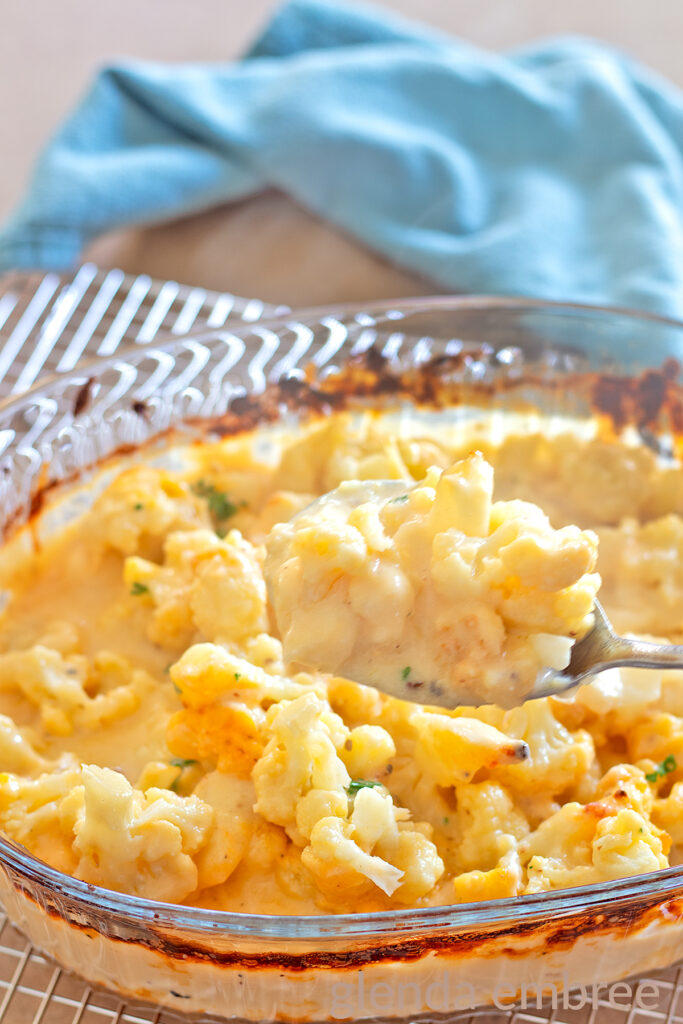 Baked Cauliflower Gratin, (Cauliflower with Cheese Sauce), Cauliflower Cheese, Cheesy Cauliflower in a clear glass baking dish with a sprinkle of chopped parsley.