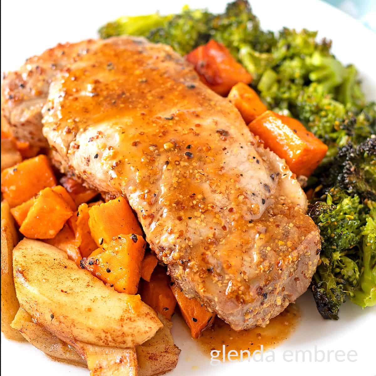 Sheet Pan Honey Mustard Pork Chops on a white plate with roasted sweet potatoes, cinnamon apples and broccoli.