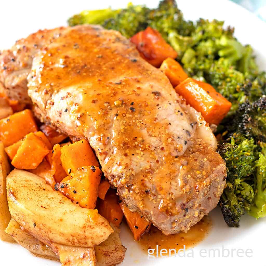 Sheet Pan Honey Mustard Pork Chops on a white plate with roasted sweet potatoes, cinnamon apples and broccoli.