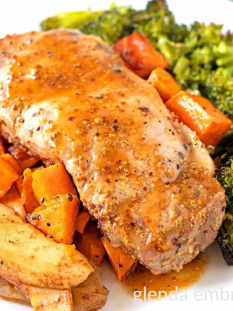 Sheet Pan Honey Mustard Pork Chops on a white plate with roasted sweet potatoes, cinnamon apples and broccoli.