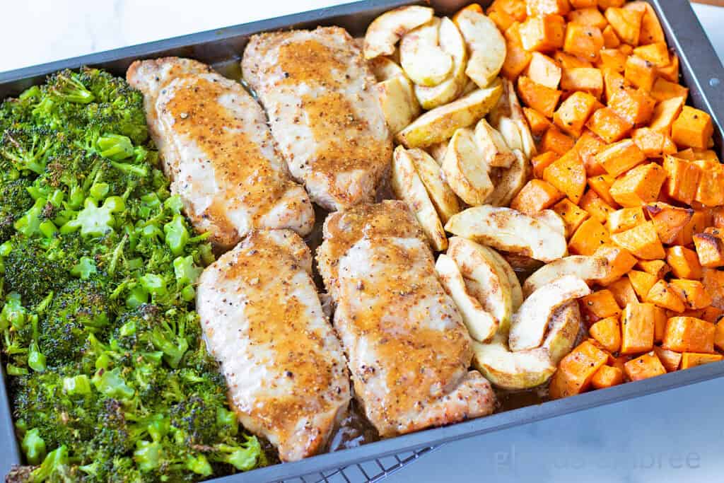 Sheet Pan Honey Mustard Pork Chops on a baking sheet with roasted sweet potatoes, cinnamon apples and broccoli.