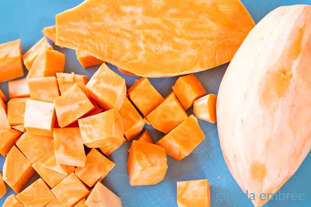 Sweet potatoes peeled and partially chopped on a cutting board.