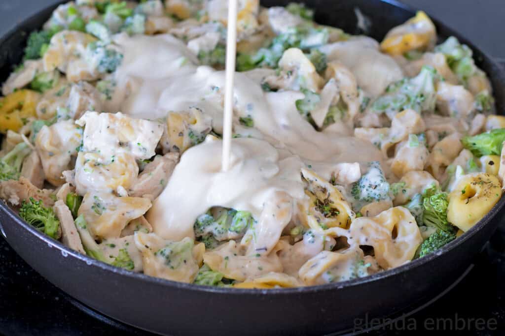 Adding Alfredo Sauce to Chicken Tortellini Casserole with Broccoli.