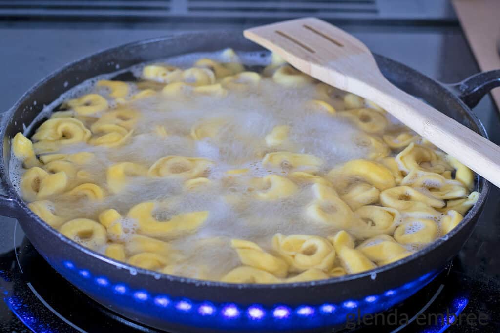 Tortellini boiling in a cast-iron skillet.