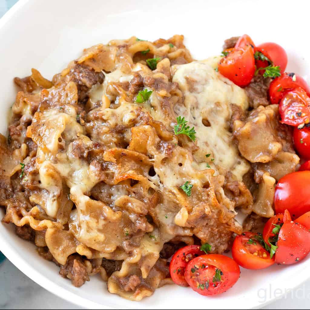 French Onion Beef and Noodles in a white dish with tomato salad.