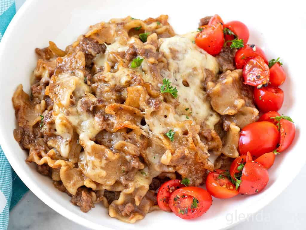 French Onion Beef and Noodles in a white dish with tomato salad.