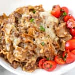 French Onion Beef and Noodles in a white dish with tomato salad.