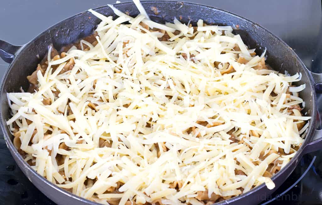 French Onion Beef and Noodle Casserole sprinkled with grated cheese in a cast iron skillet on the stovetop.