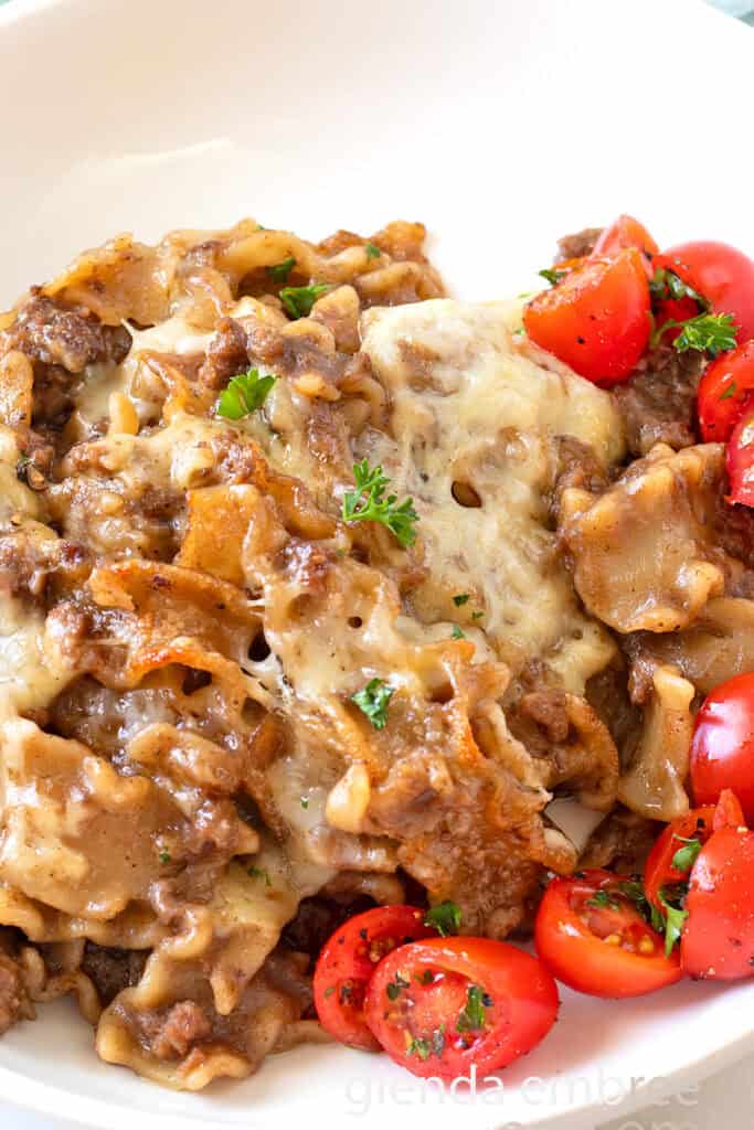 French Onion Beef and Noodles in a white dish with tomato salad.