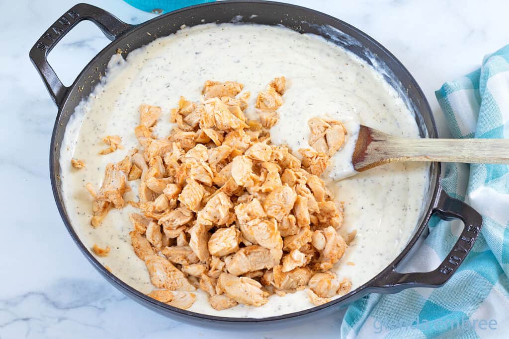 Adding precooked and chopped chicken to chicken tetrazzini sauce.