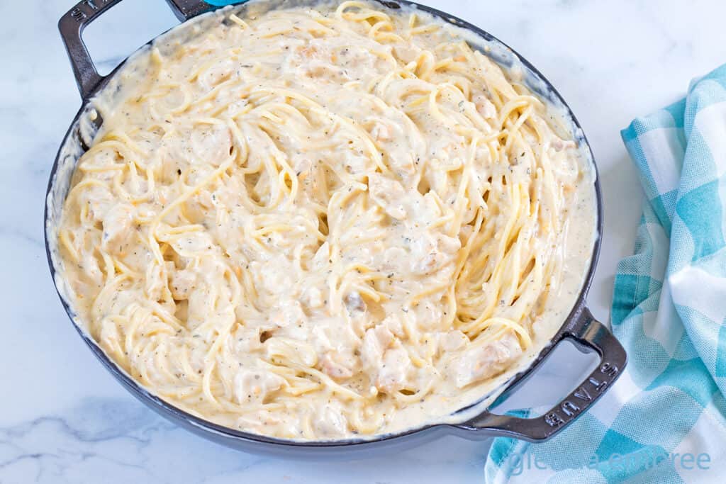 Adding precooked spaghetti noodles to chicken tetrazzini sauce.
