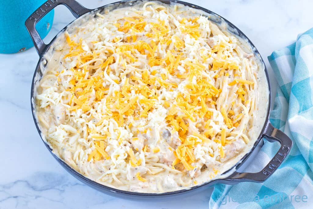 Topping chicken tetrazzini casserole with grated cheese to get it ready for the oven.