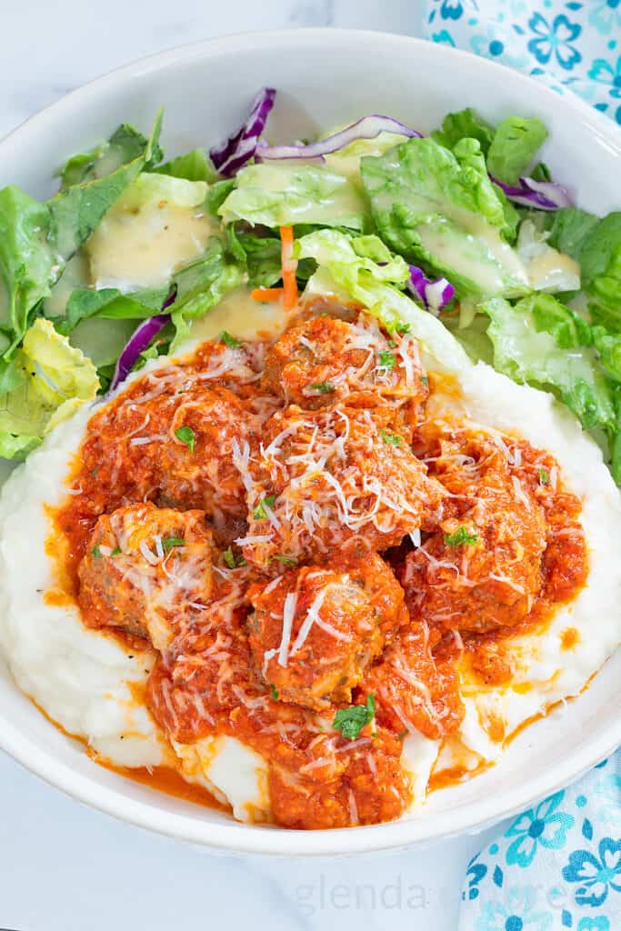 Porcupine Meatballs and Tomato Gravy over mashed potatoes on a white plate with a tossed salad.