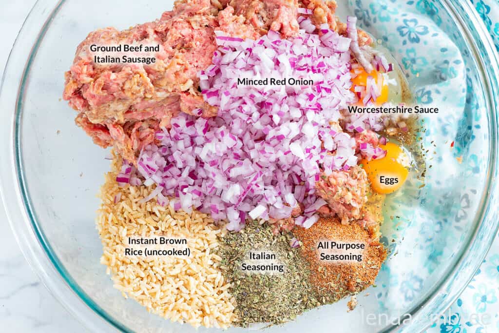 Ingredients for porcupine meatballs in a clear glass bowl: ground meat, dry instant rice, eggs, Worcestershire sauce, All Purpose Seasoning and Italian seasoning.