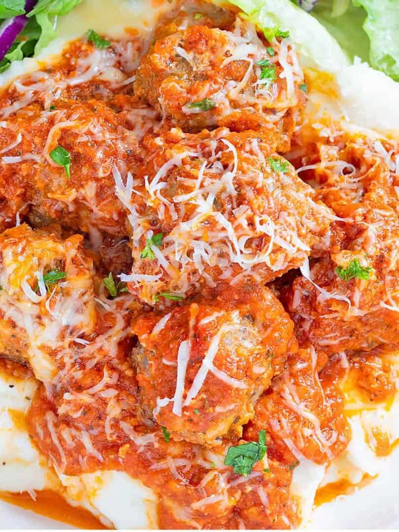Porcupine Meatballs and Tomato Gravy over mashed potatoes on a white plate with a tossed salad.