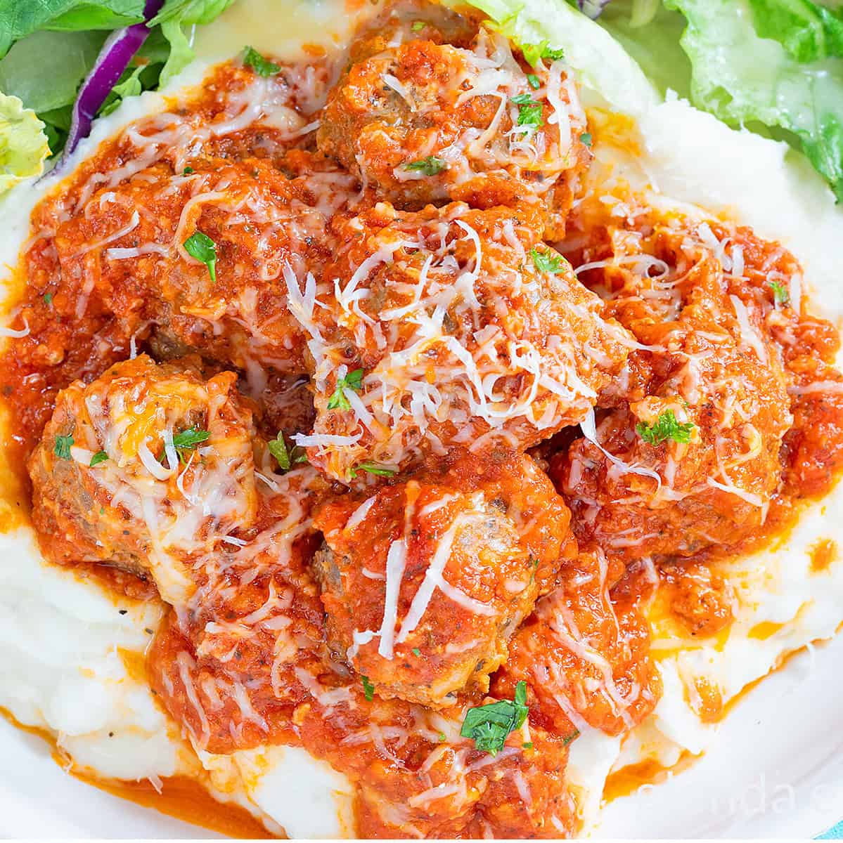 Porcupine Meatballs and Tomato Gravy over mashed potatoes on a white plate with a tossed salad.