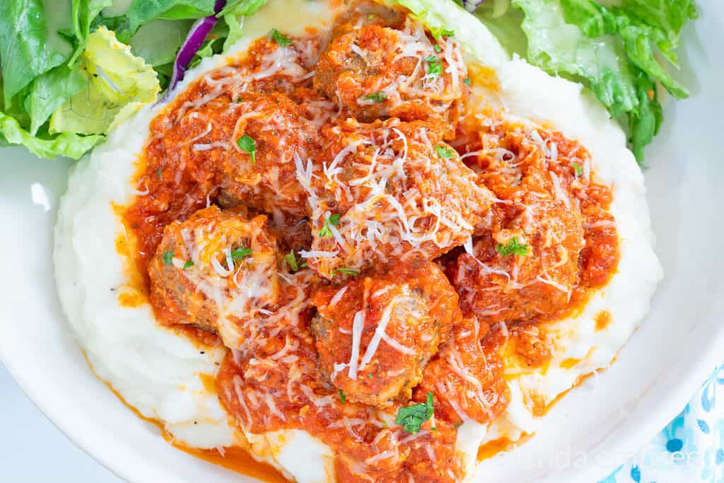 Porcupine Meatballs and Tomato Gravy over mashed potatoes on a white plate with a tossed salad.