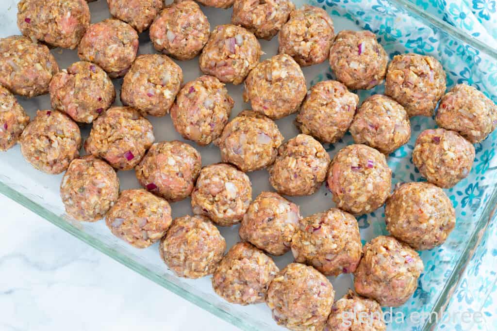 Raw meatballs rolled and arranged in a clear glass baking dish.