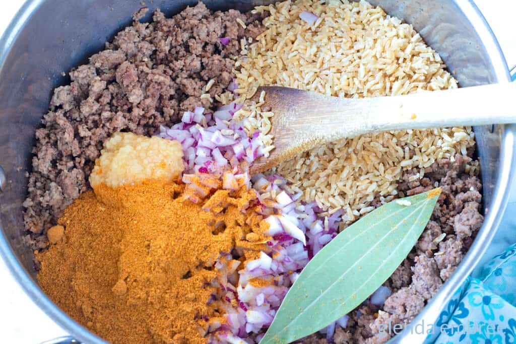 Browned ground beef, dry instant brown rice, taco seasoning, minced red onion and bay leaf in a soup pot.