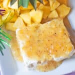 Jezebel Sauce over Cream Cheese on a white rectangular stoneware platter with a pineapple stem and fresh pineapple chunks.