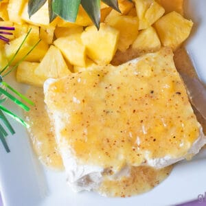 Jezebel Sauce over Cream Cheese on a white rectangular stoneware platter with a pineapple stem and fresh pineapple chunks.