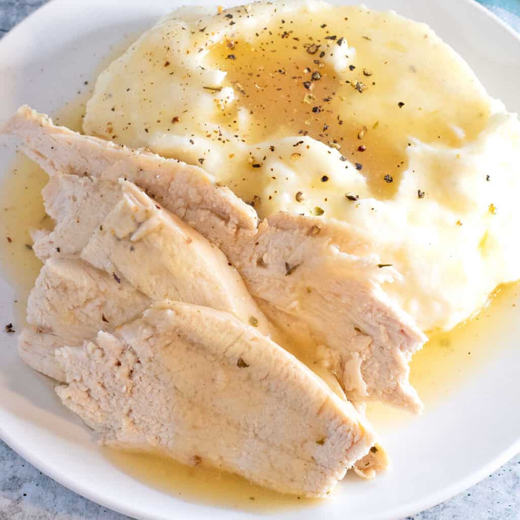 Convection Oven Turkey in a Bag sliced and arranged on a white plate with mashed potatoes and gravy.