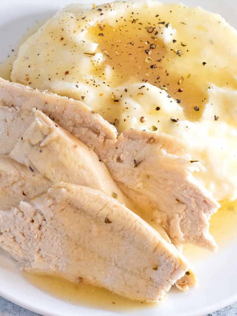Convection Oven Turkey in a Bag sliced and arranged on a white plate with mashed potatoes and gravy.