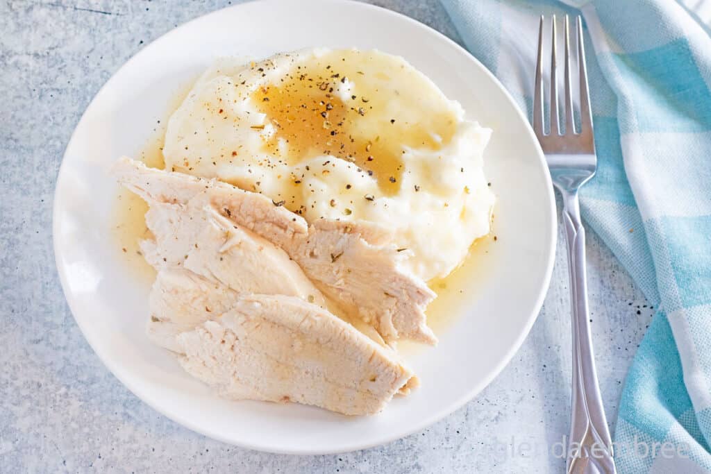 Convection Oven Turkey in a Bag sliced and arranged on a white plate with mashed potatoes and gravy.