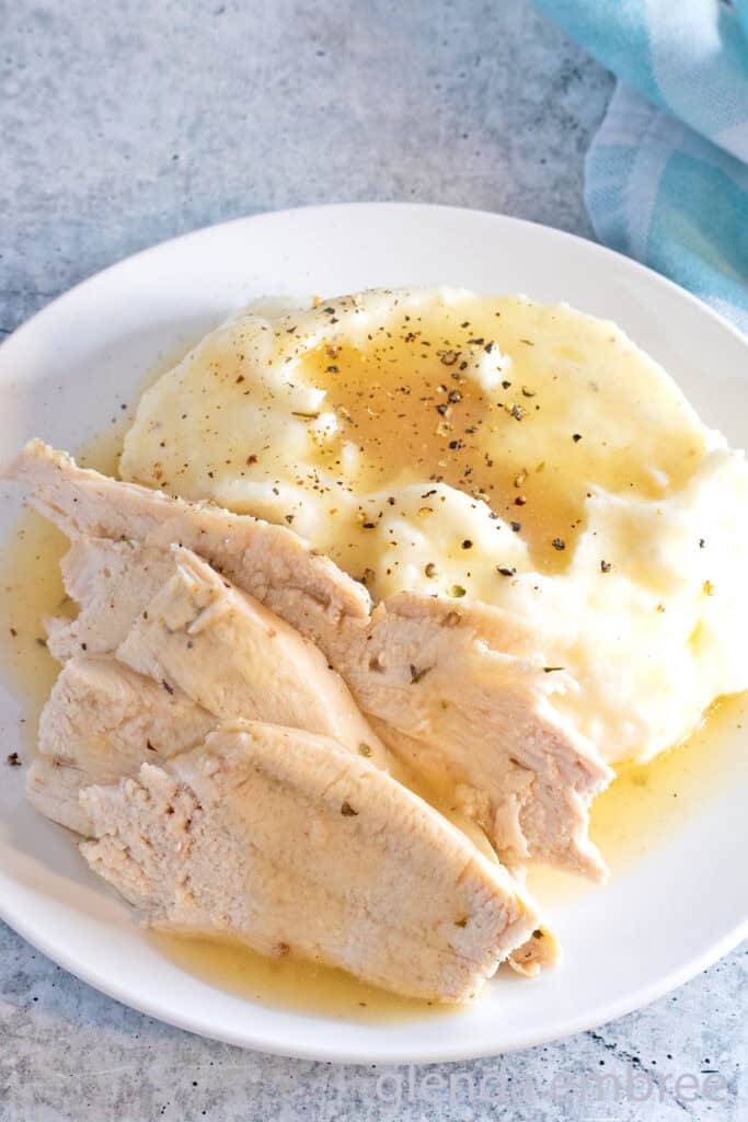 Convection Oven Turkey in a Bag sliced and arranged on a white plate with mashed potatoes and gravy.