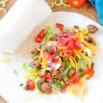 Ground Beef Taco Meat, sour cream, grated Cheddar, and pico de gallo in the center of a flour tortilla to make Ground Beef Tacos.