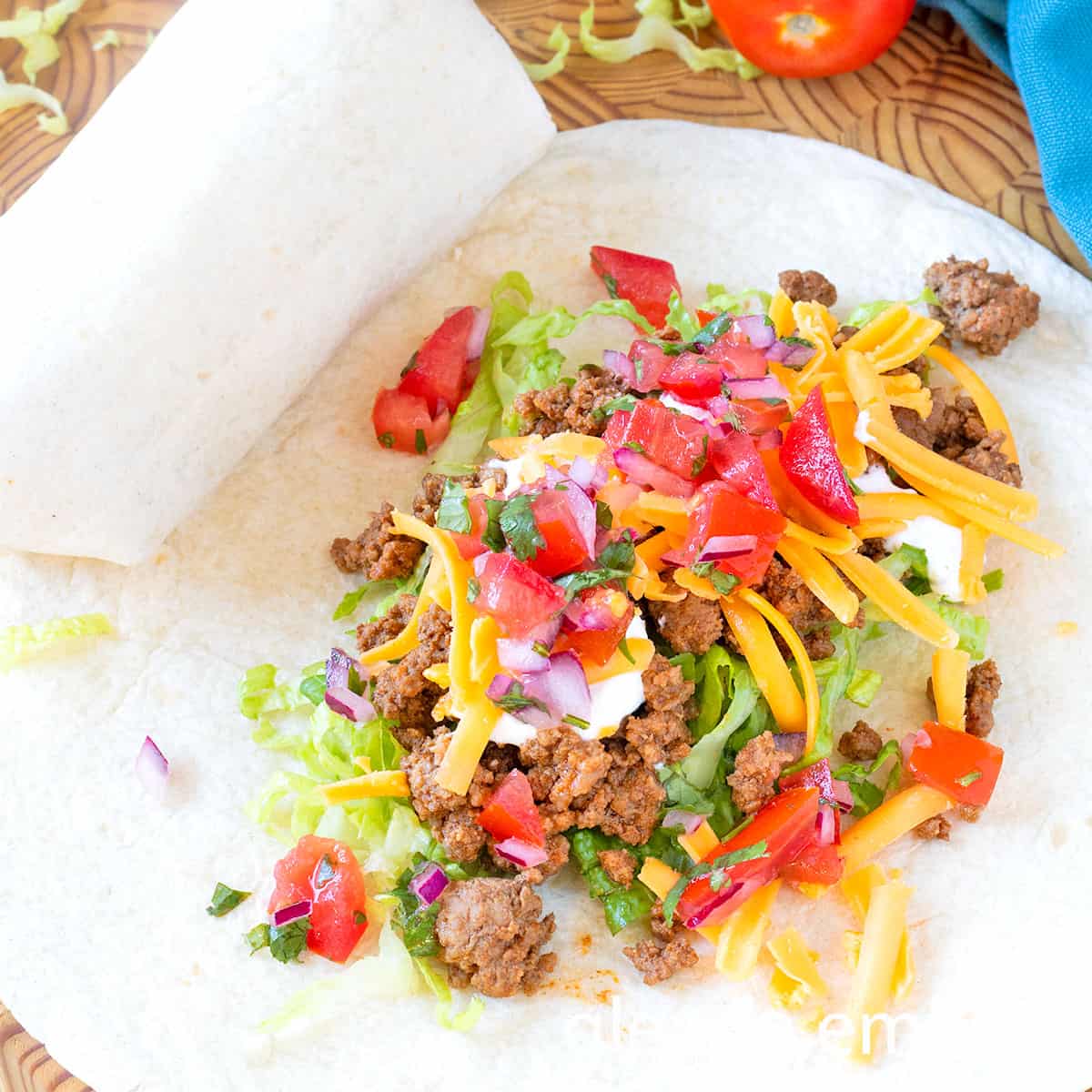 Ground Beef Taco Meat, sour cream, grated Cheddar, and pico de gallo in the center of a flour tortilla to make Ground Beef Tacos.