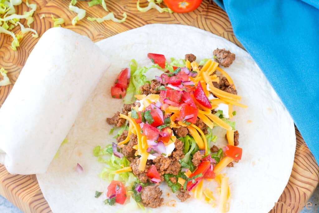 Ground Beef Taco Meat, sour cream, grated Cheddar, and pico de gallo in the center of a flour tortilla to make Ground Beef Tacos (Soft Tacos).