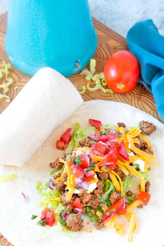Ground Beef Taco Meat, sour cream, grated Cheddar, and pico de gallo in the center of a flour tortilla to make Ground Beef Tacos (Soft Tacos).