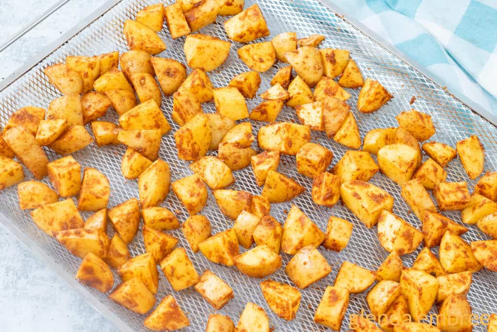 Raw taco potatoes prepped and spread on an oven-sized air fryer rack on a concrete countertop.