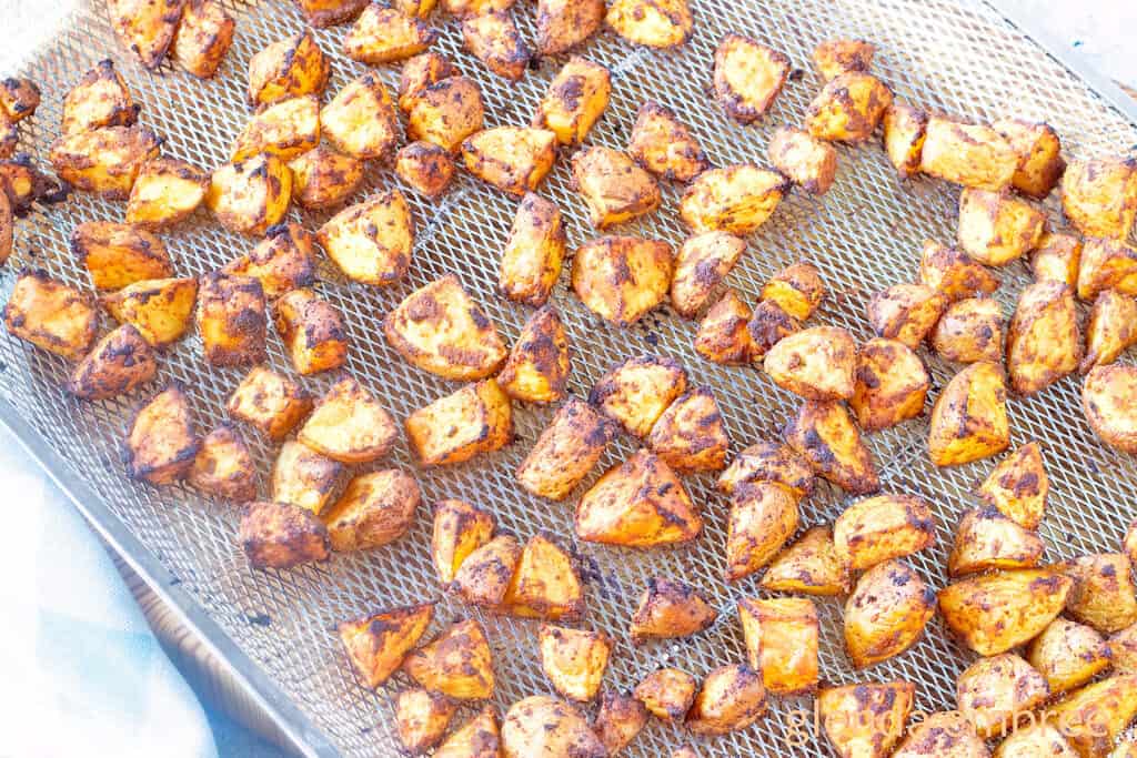 Roasted taco potatoes prepped and spread on an oven-sized air fryer rack on a concrete countertop.