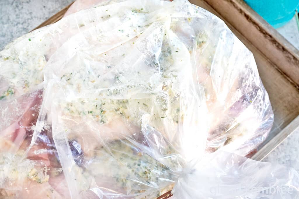 Raw turkey covered in compound butter and resting on onions, carrots, celery, and bay leaf all in an oven roasting bag ready for cooking in a convection. oven.