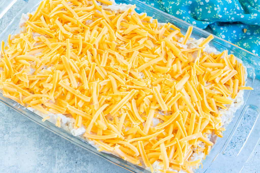 Adding the cheese layer in a clear glass baking dish as Chicken Casserole is assembled.