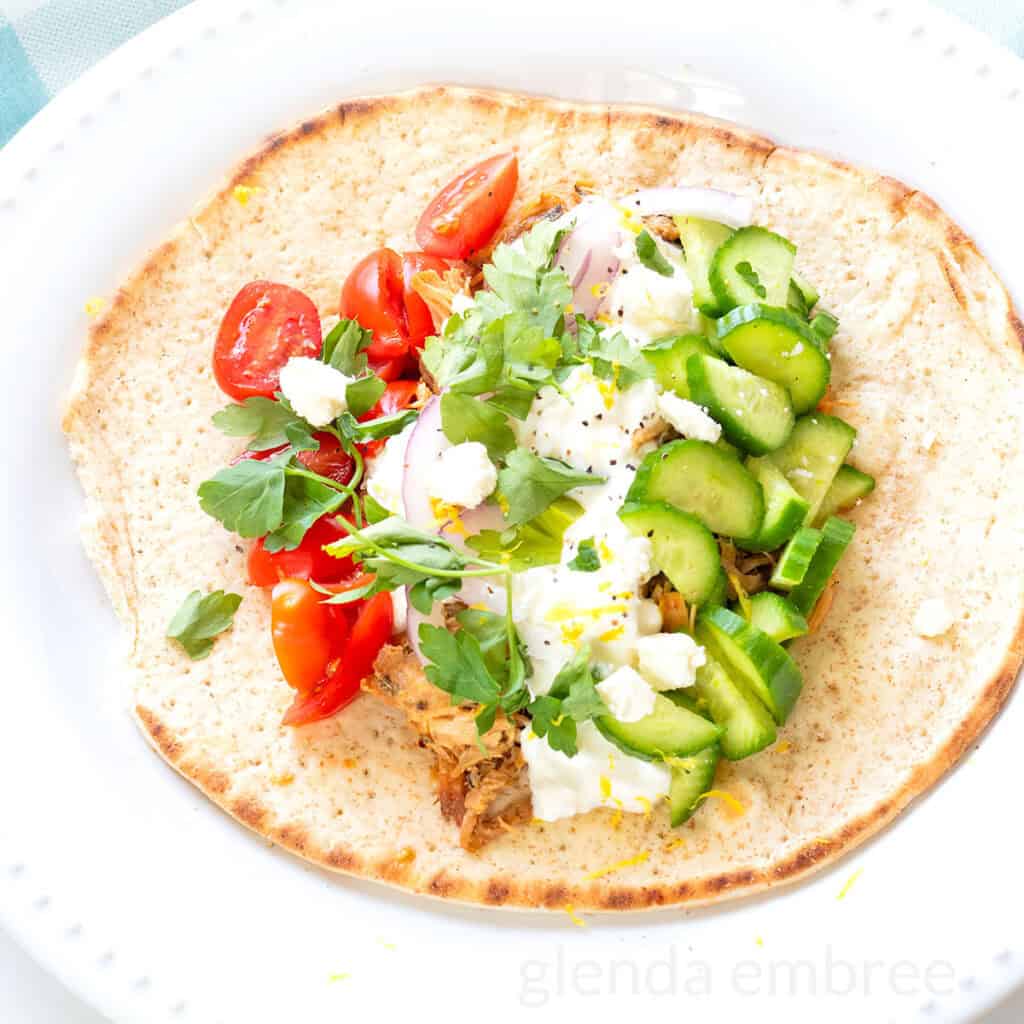 Cheats pork souvlaki on a pita wrap with cottage cheese, sliced cucumbers, slivered red onion, chopped tomatoes and fresh parsley.