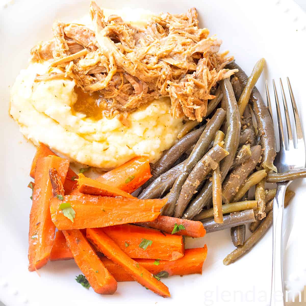 Slow Cooker Pork Roast over mashed potatoes on a white plate with green beans and carrots.