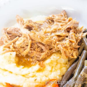 Slow Cooker Pork Roast on a white plate with mashed potatoes, carrots and green beans.
