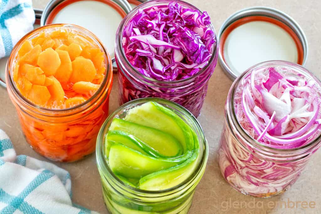 Sliced vegetables in mason jars with pickling brine—Quick pickled red onions, quick pickled cucumbers and quick pickled cabbage.
